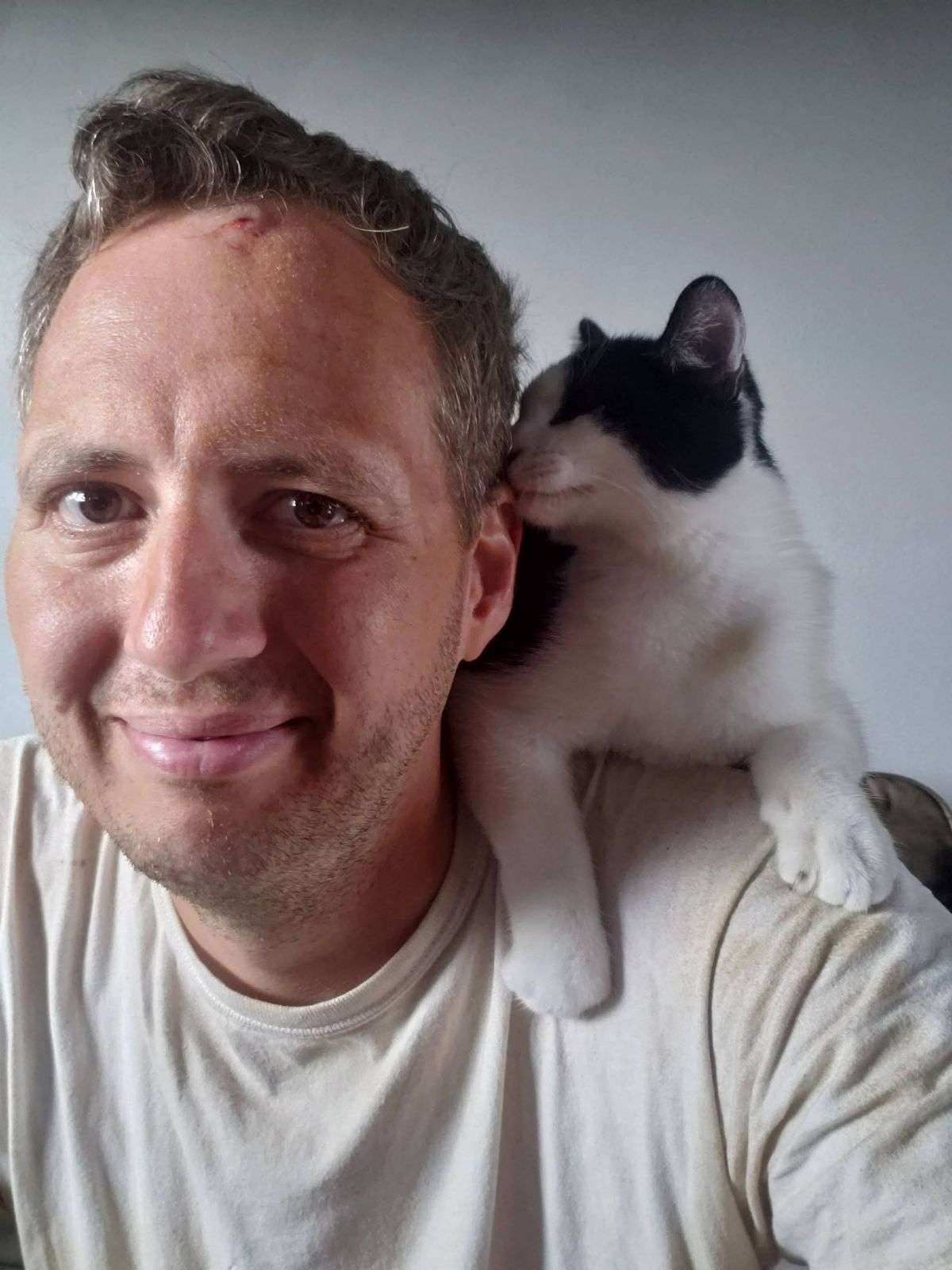 black and white kitten perches on man's shoulder.