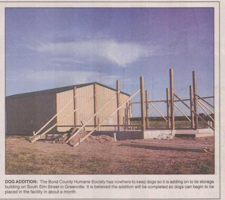 newspaper photo with caption, dog shelter addition under construction with foundation poured and posts installed.