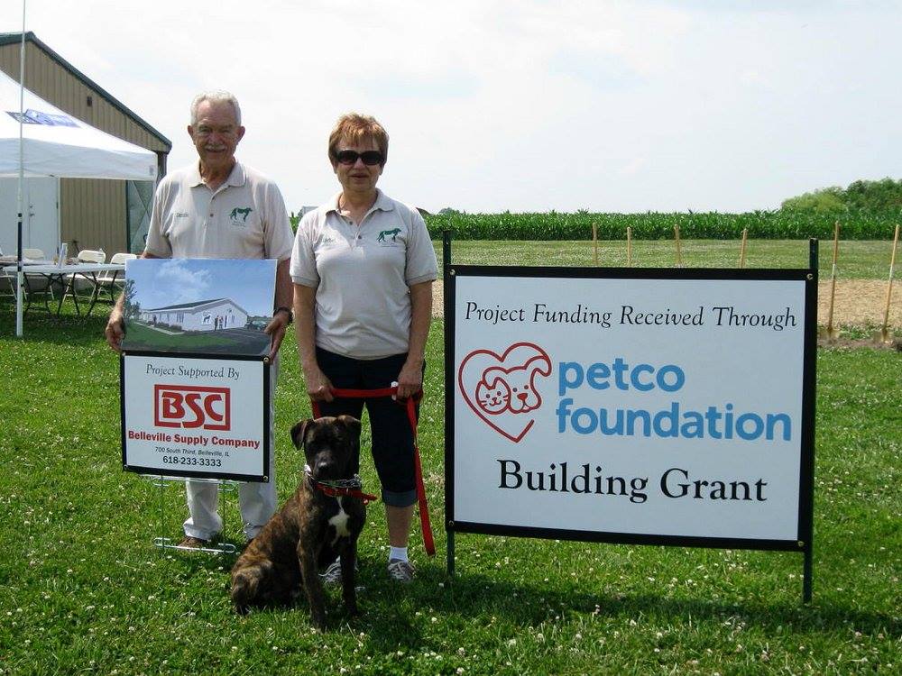 Dennis and Rachel Hundsdorfer pose in front of shelter site with artist sketch, Belleville Supply Company sign and Petco Foundation sign