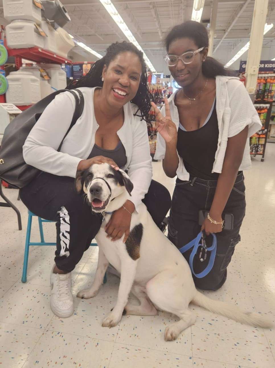 large white and black dog inside a retail store with two smiling women with dark skin and hair wearing black pants and white shirts